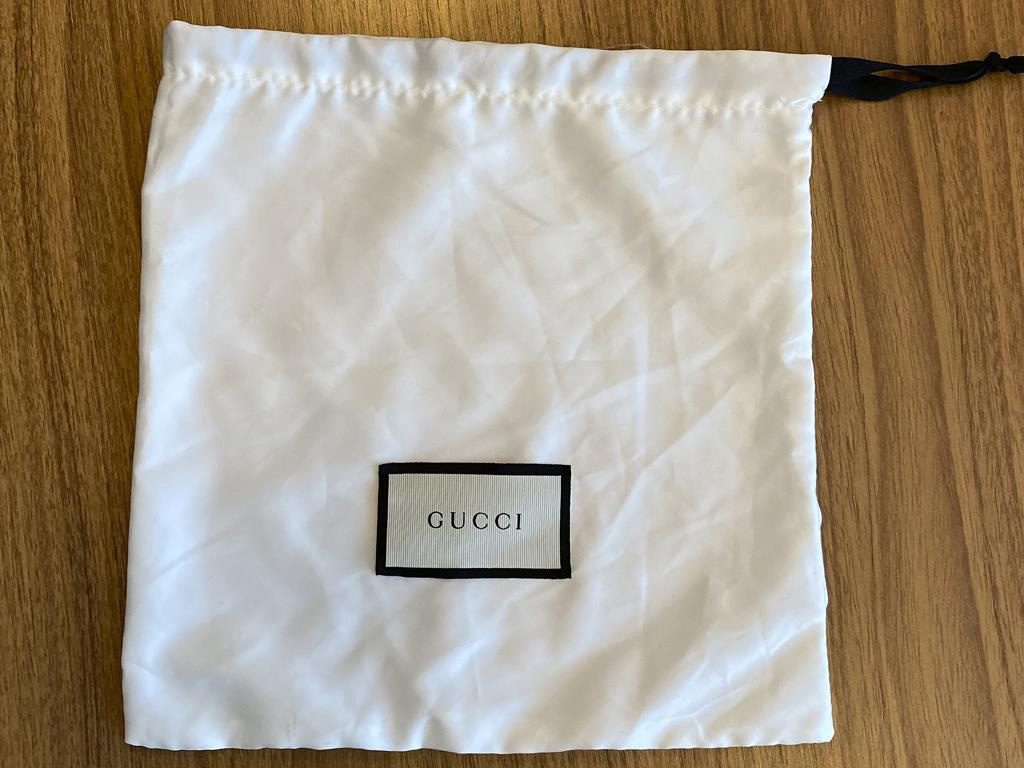 A dust de cetim branca com tag do nome Gucci está começando a acompanhar com muita frequência bolsas e sapatos da marca.